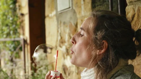 A woman blows a large bubble as a tiny child's hand reaches up to burst it. Stock Footage 170349824