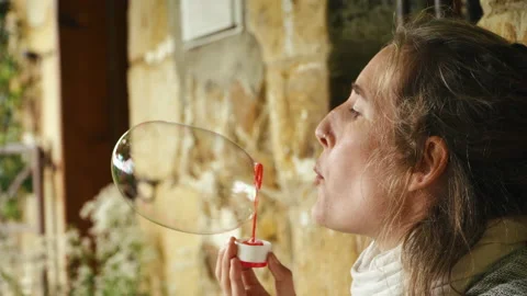 A woman blows a large bubble as a tiny child's hand reaches up to burst it. Stock Footage 171262944