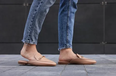 Woman in blue jeans and fashionable slippers walking on city street, closeup Stock Photos