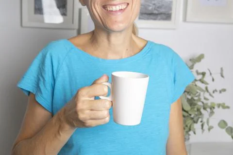 Woman in blue t-shirt drinking white cup of coffee or tea in the morning and in  Stock Photos