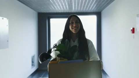 Woman with a box of things is walking down the corridor to the new office Stock Footage 232478368