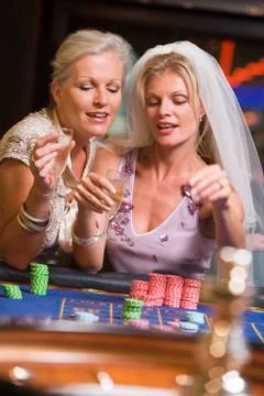Woman in bridal veil with another woman in casino playing roulette and smiling Stock Photos