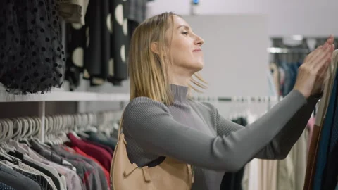 Woman browsing clothes in store with handbag showing clothing shopping fashion Stock Footage 346735599