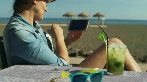 Woman browsing internet on smartphone while sitting on the beach, steadycam shot Stock-Footage 60133904
