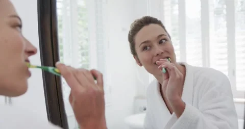 Woman brushing teeth looking in mirror in bathroom, slow motion Stock Footage 342017945