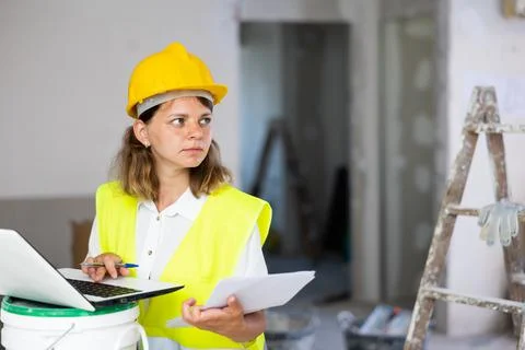 Woman builder checking documentation, using laptop Stock Photos