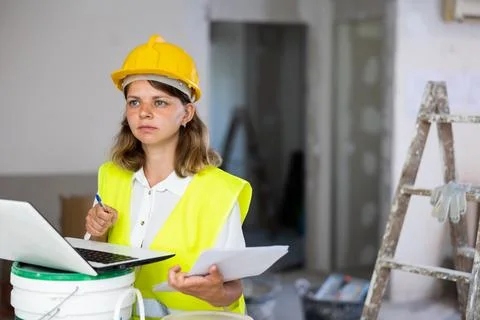Woman builder checking documentation, using laptop Fotos de archivo