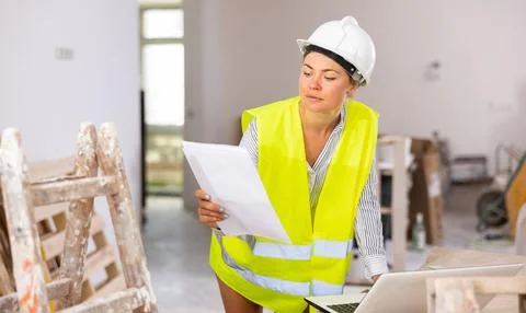 Woman builder checking documentation, using laptop Foto stock