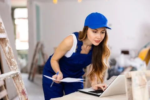 Woman builder checking documentation, using laptop Fotos de archivo