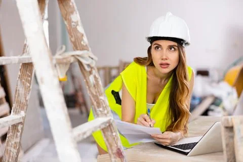 Woman builder checking documentation, using laptop Stock Photos