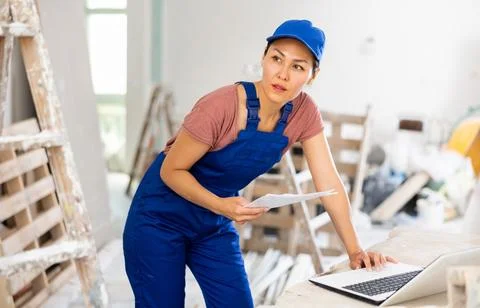 Woman builder checking documentation, using laptop 写真素材