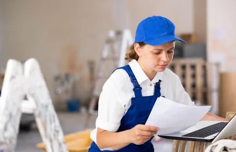 Woman builder checking documentation, using laptop Foto stock
