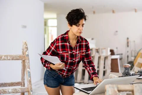 Woman builder checking project documentation and using laptop while working 스톡 사진