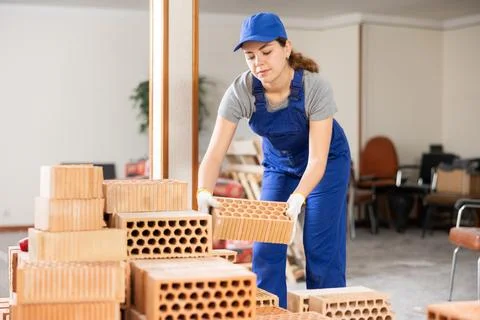 Woman builder stacking red bricks inside building under construction Stock Photos
