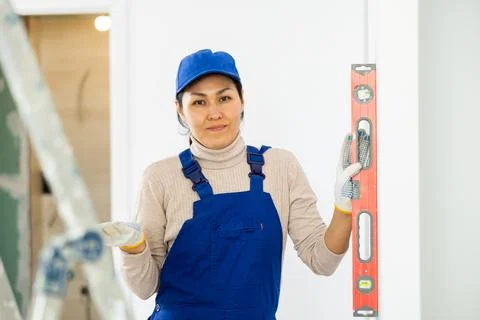Woman builder using building level measures the vertical of wall Fotos de archivo
