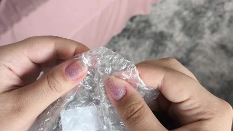 Woman bursts bubbles on a packaging bubble wrap, trying to calm down. Burst the Stock Footage 314974563