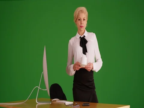 Woman in business attire at her desk with coffee in her hand on green screen Stock Footage