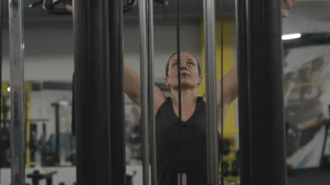 A woman in a cable machine performs seated lat pulldowns, developing her back mu Stock Footage 255314489