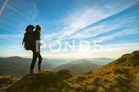 The woman with a camping backpack standing on the rock with a picturesque sun Stock Photos