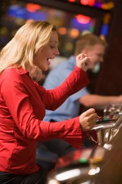 Woman in casino excited playing slot machine with people in background Stock Photos