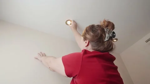 Woman changing or checking a ceiling light bulb in her home. Stock Footage 144089796