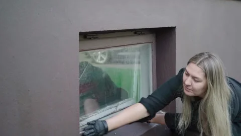 Woman Checking Damaged Basement Window Frame for Home Repair or Replacement Stock Footage 340075659