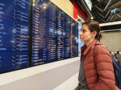 Woman checking flight schedule on digital board at airport terminal Stock Photos