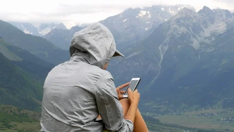 A woman checking her phone while sitting on top of a hill overlooking mountains Vídeos de archivo 94328332