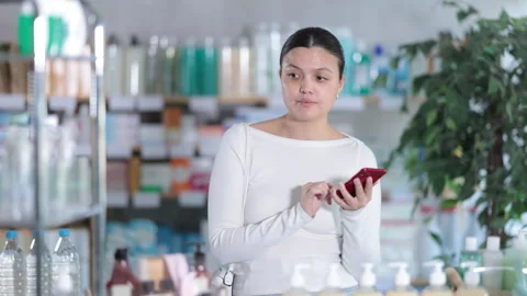 Woman checking list of needed items on phone while shopping at pharmacy Stock Footage 312633278