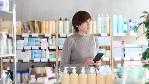 Woman checking list of needed items on phone while shopping at drugstore Stock Footage 322114173