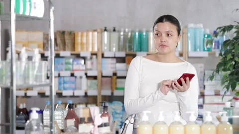 Woman checking list of needed items on phone while shopping at pharmacy Stock Footage 322115845