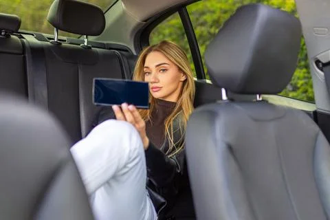 Woman checking makeup in handheld mirror while sitting in back seat of car Fotos de archivo