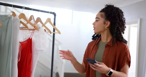 Woman checking phone, glancing at rack, lifting white top in dressing area while Vídeo Stock 344341772