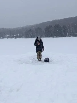 Woman Checking Phone While Ice Fishing on a Snowy Frozen Lake Fotos Stock