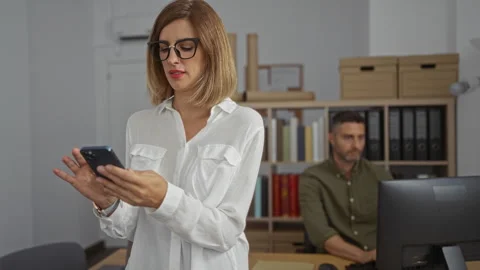 Woman checking phone while man works on computer in an office setup with bo.. Stock Footage 283556268