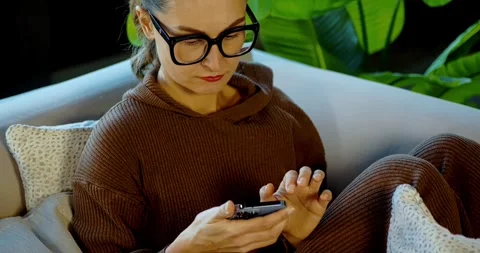 Woman Checking Smartphone While Sitting on a Cozy Couch Vídeos de archivo 324583082