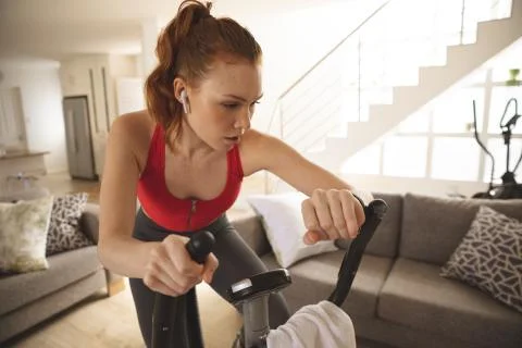 Woman checking time while exercising on stationary bike at home Stock Photos