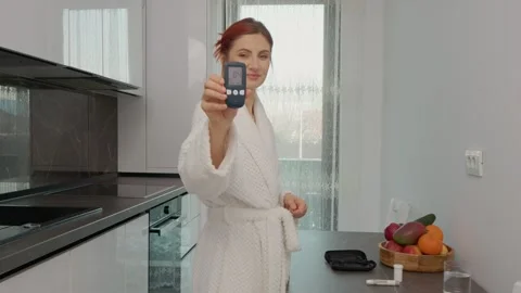 Woman checks glucometer reading in kitchen for good diabetes result Stock Footage 346704172