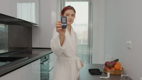 Woman checks glucometer reading in kitchen and reveals high blood sugar level Stock Footage 346704188