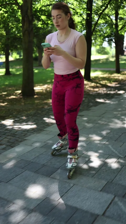 Woman checks smartphone while rollerblading through a green park Video stock 341476299
