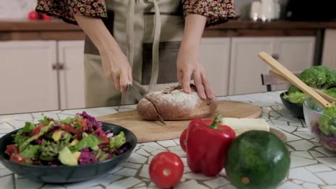 Woman chef cutting bread on kitchen table. Preparing healthy meal in a home Stock Footage 291297762