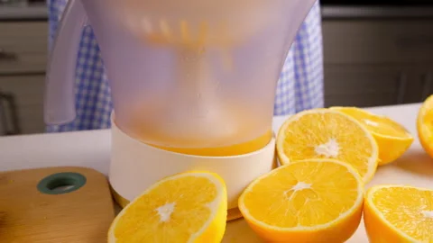 Woman chef squeezing oranges using electric juicer in kitchen at home. Stock Footage 312985612