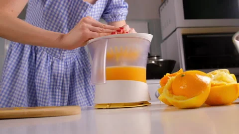 Woman chef squeezing oranges using electric juicer in kitchen at home. Stock Footage 312985866