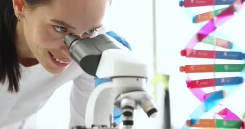 Woman chemist looking through microscope near dna molecule layout 4k movie slow Video stock 165671240