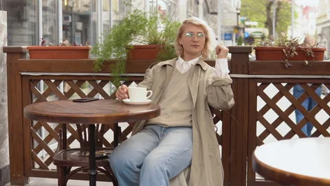 Woman chillls out while resting sitting with a cup of coffee at a table on the Stock Footage 155176190