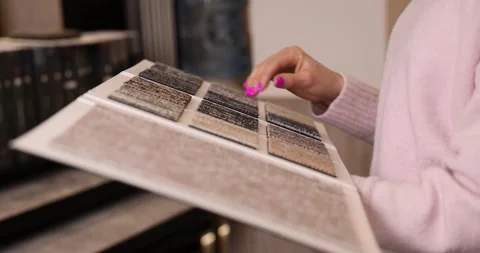 Woman choosing carpet design from samples book in flooring shop Stock Footage 330673192