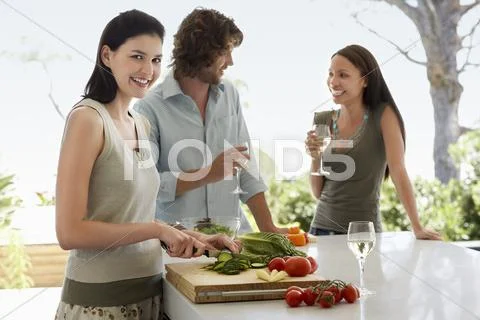 Woman Chopping Vegetables With Friends Communicating At Kitchen Counter Stock Photos