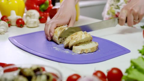 Woman chops bread into slices on violet cutting board Stock Footage 231908753