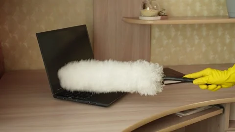 A woman in cleaning gloves is using a duster to clean dust from her desk and Stockbeeldmateriaal 308583457