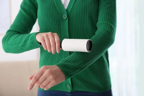Woman cleaning green jacket with lint roller indoors, closeup Stock Photos